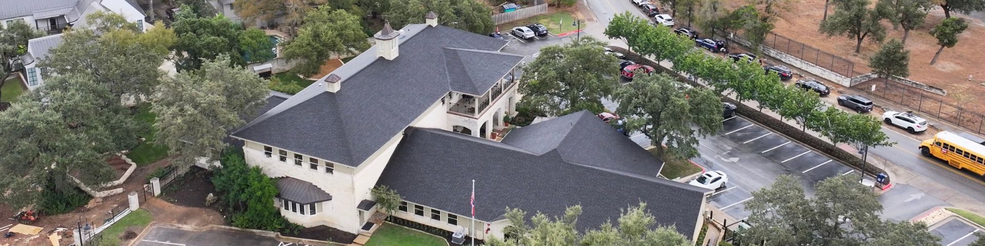 Aerial view of the West Bank Community Library in Austin, Texas, featuring a newly installed IKO® Dynasty® shingle roof in Glacier surrounded by trees and residential neighborhood streets.